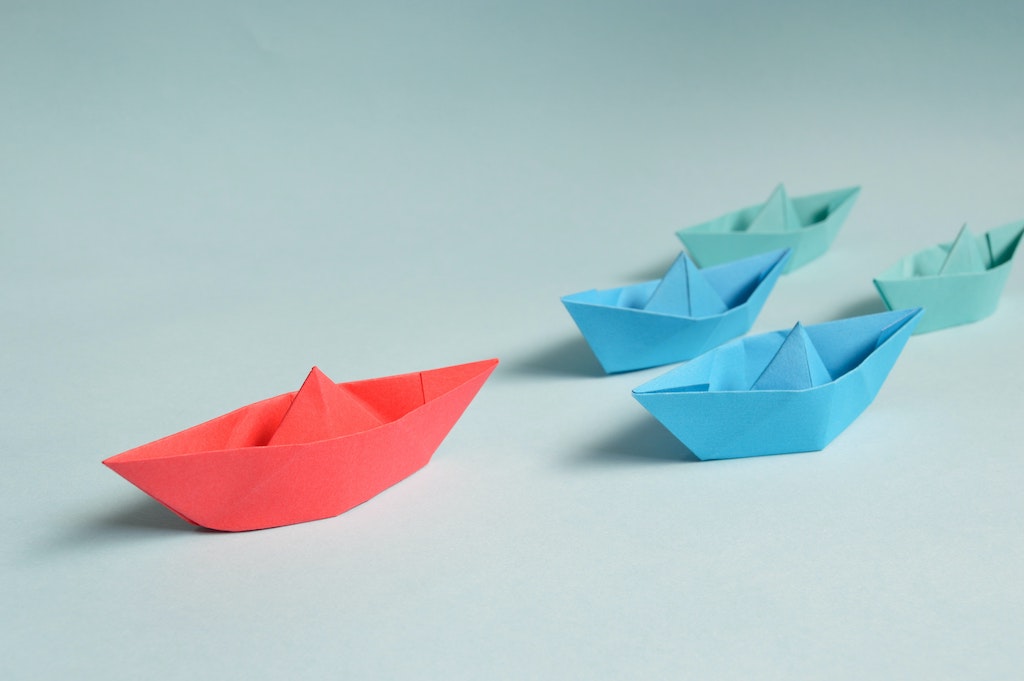 three small ships made by sheets of paper with the red one, leading the way